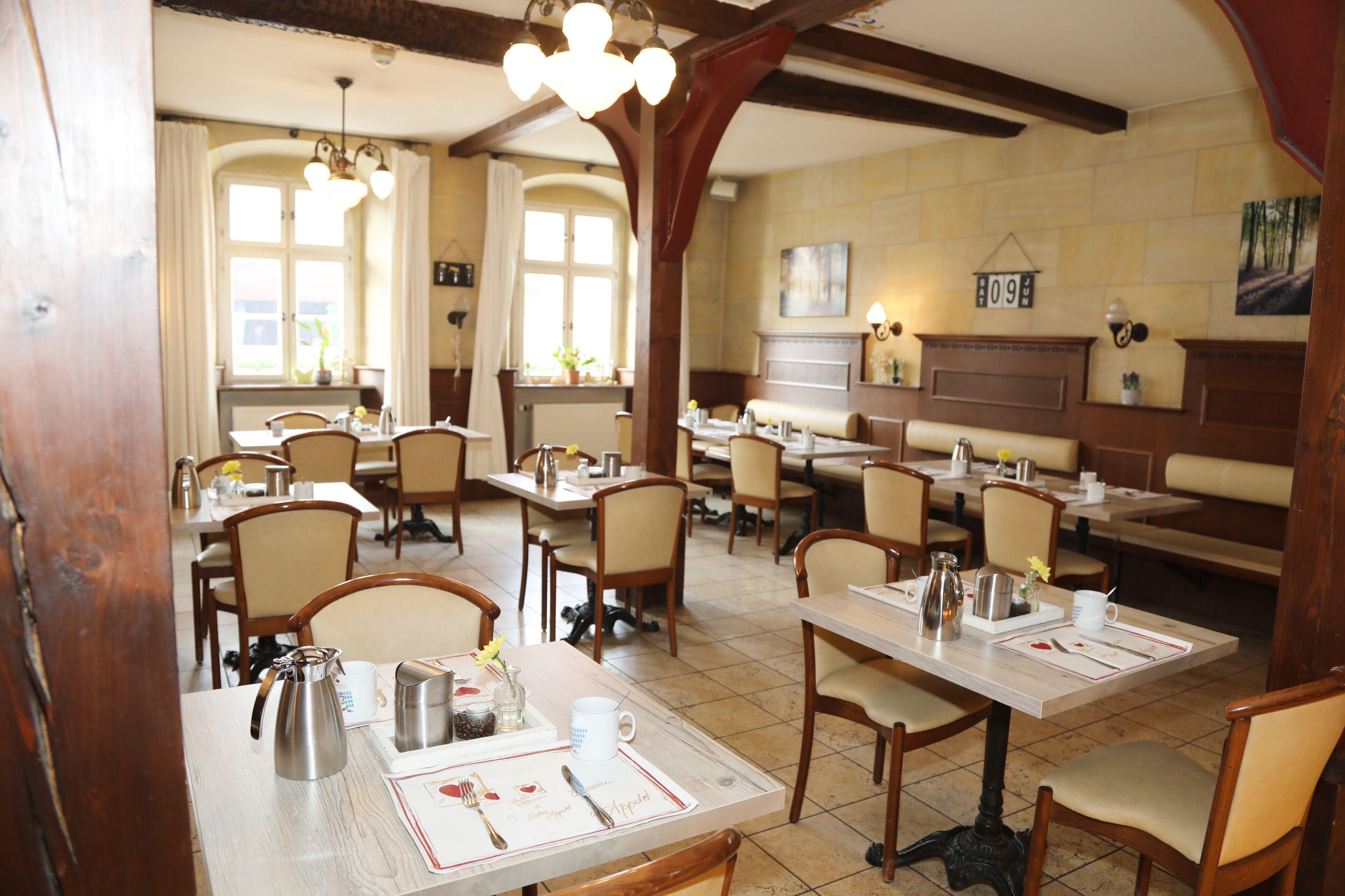 A restaurant with multiple tables, chairs, and a variety of table settings including plates, cutlery, and glasses.