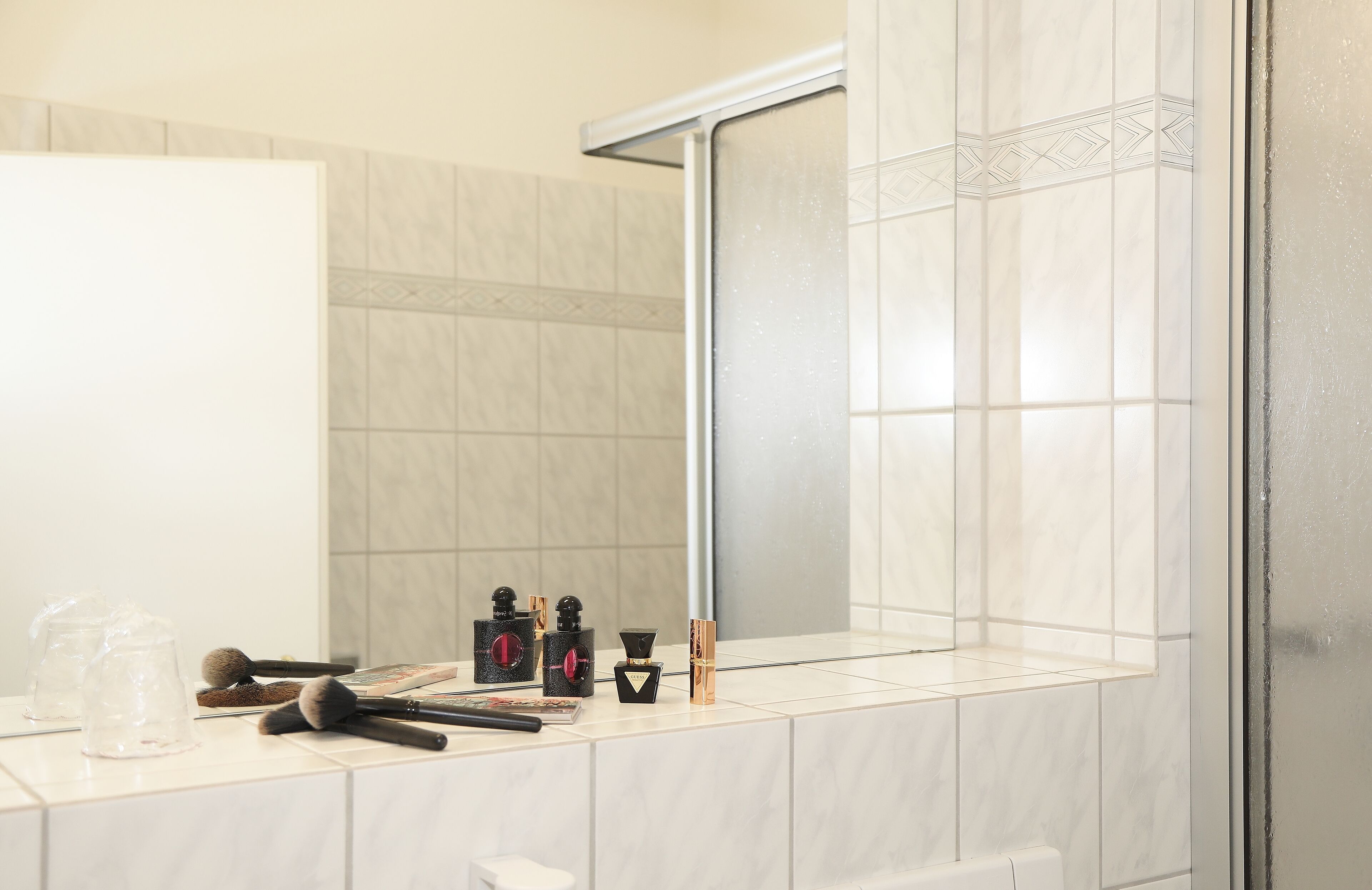 Un baño con pared de azulejos blancos, un espejo y una ventana.