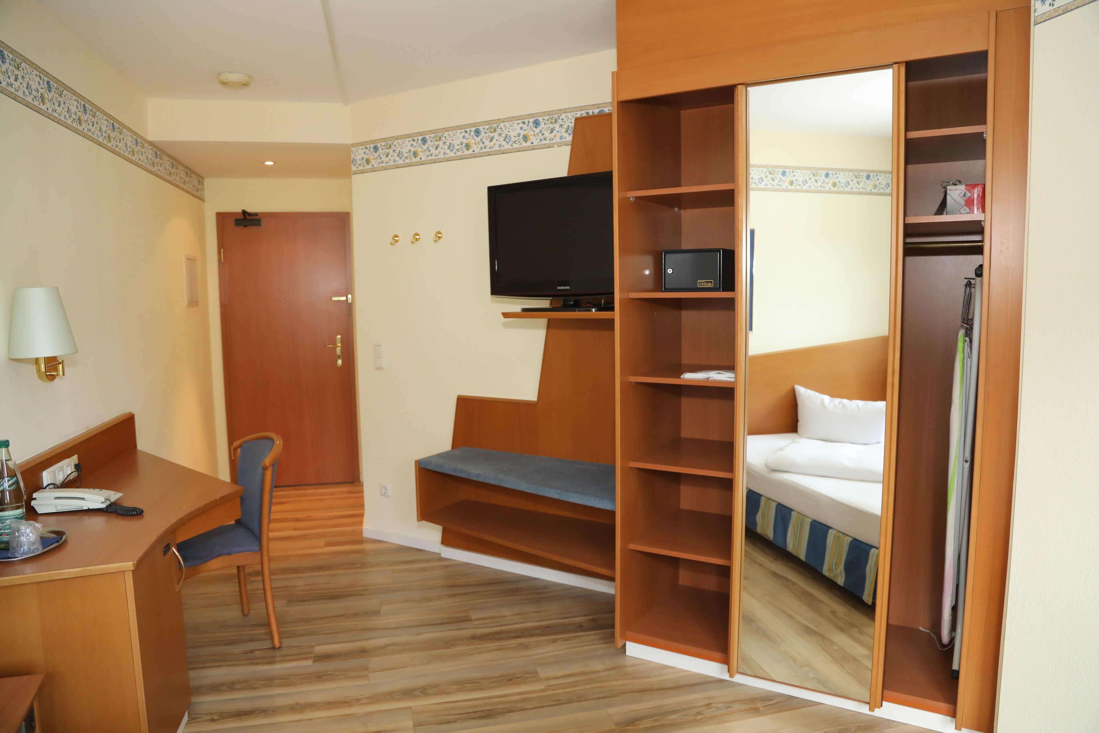 A hotel room with a desk, chair, television, and a bed with a small closet.
