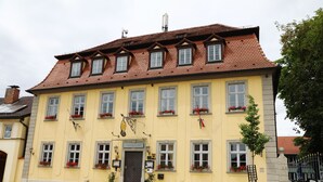 Ein gelbes Gebäude mit rotem Ziegeldach, zahlreichen Fenstern und Blumenkästen.