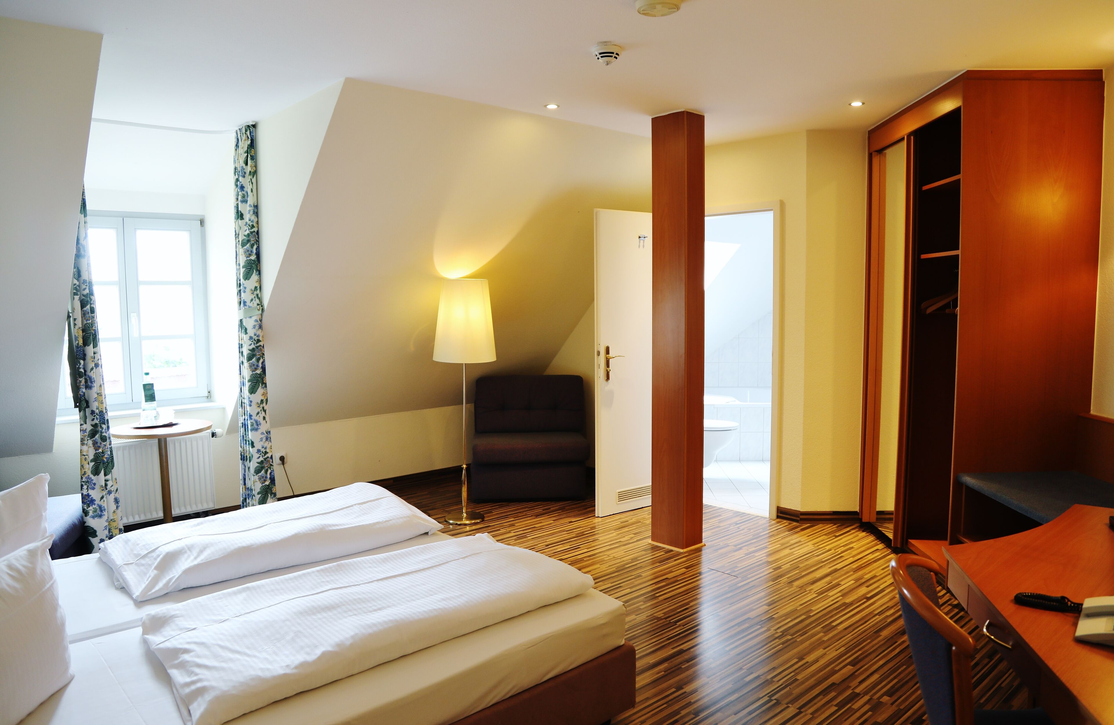 Una habitación de hotel con cama, escritorio, silla, armario y lámpara.