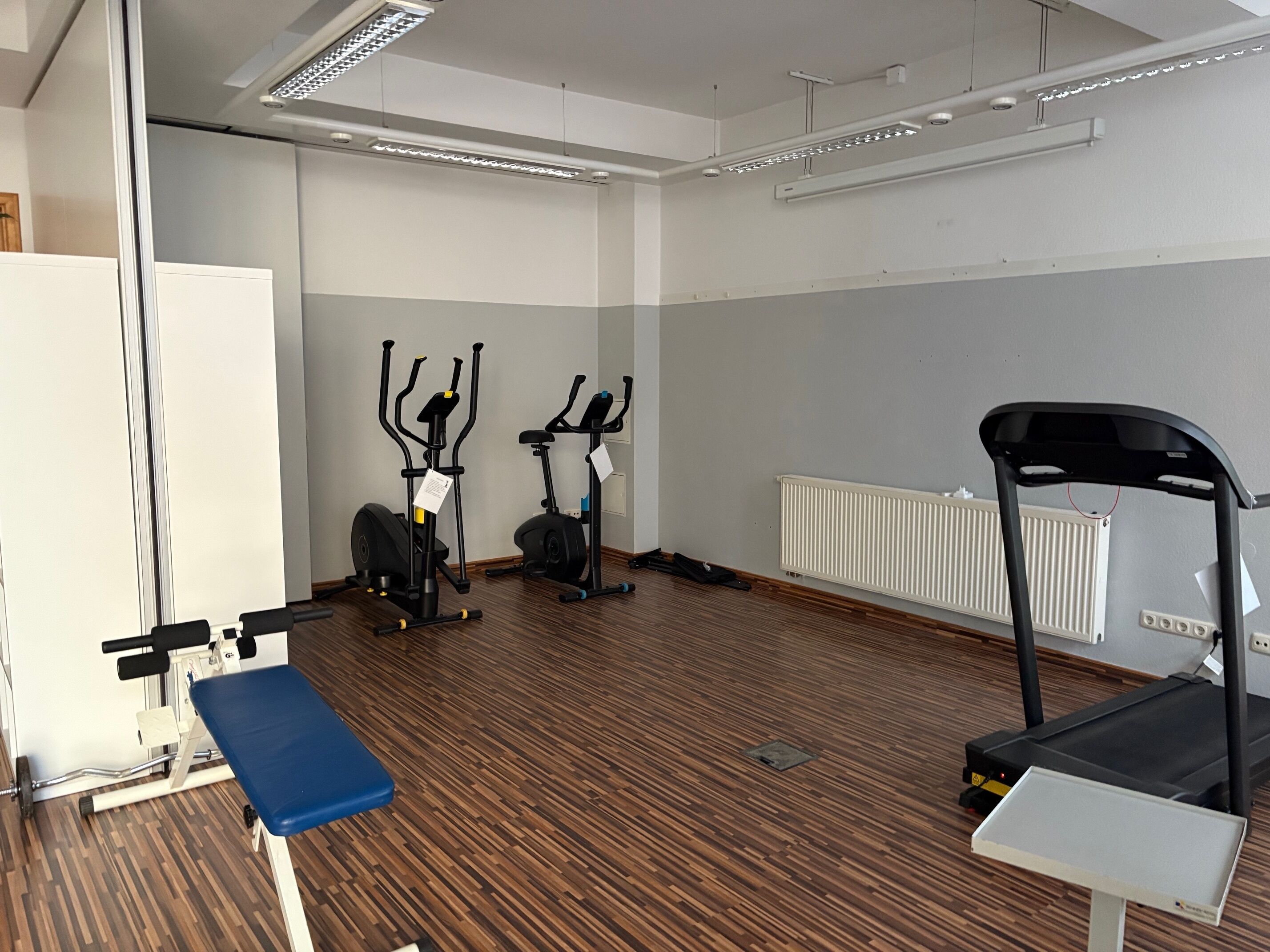 A gym with exercise equipment, a blue bench, and a treadmill.