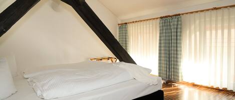 Un dormitorio con cama, vigas de madera, cortinas blancas y suelo de madera.