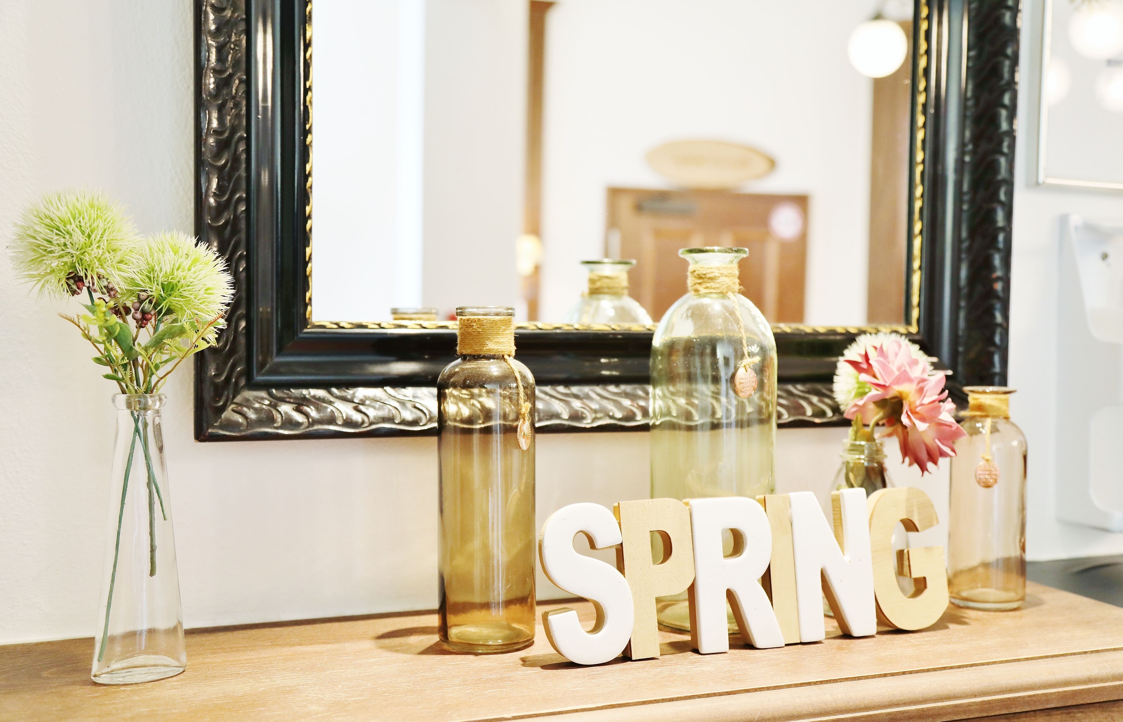 A wooden shelf with glass bottles, a vase with green plants, and the word "SPRING" in wooden letters.