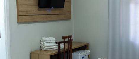 Een hotelkamer met een flatscreen-tv bevestigd aan een wand van houten panelen, een klein houten bureau met een stoel, een koelkast en twee bedden met beddengoed met een patroon.