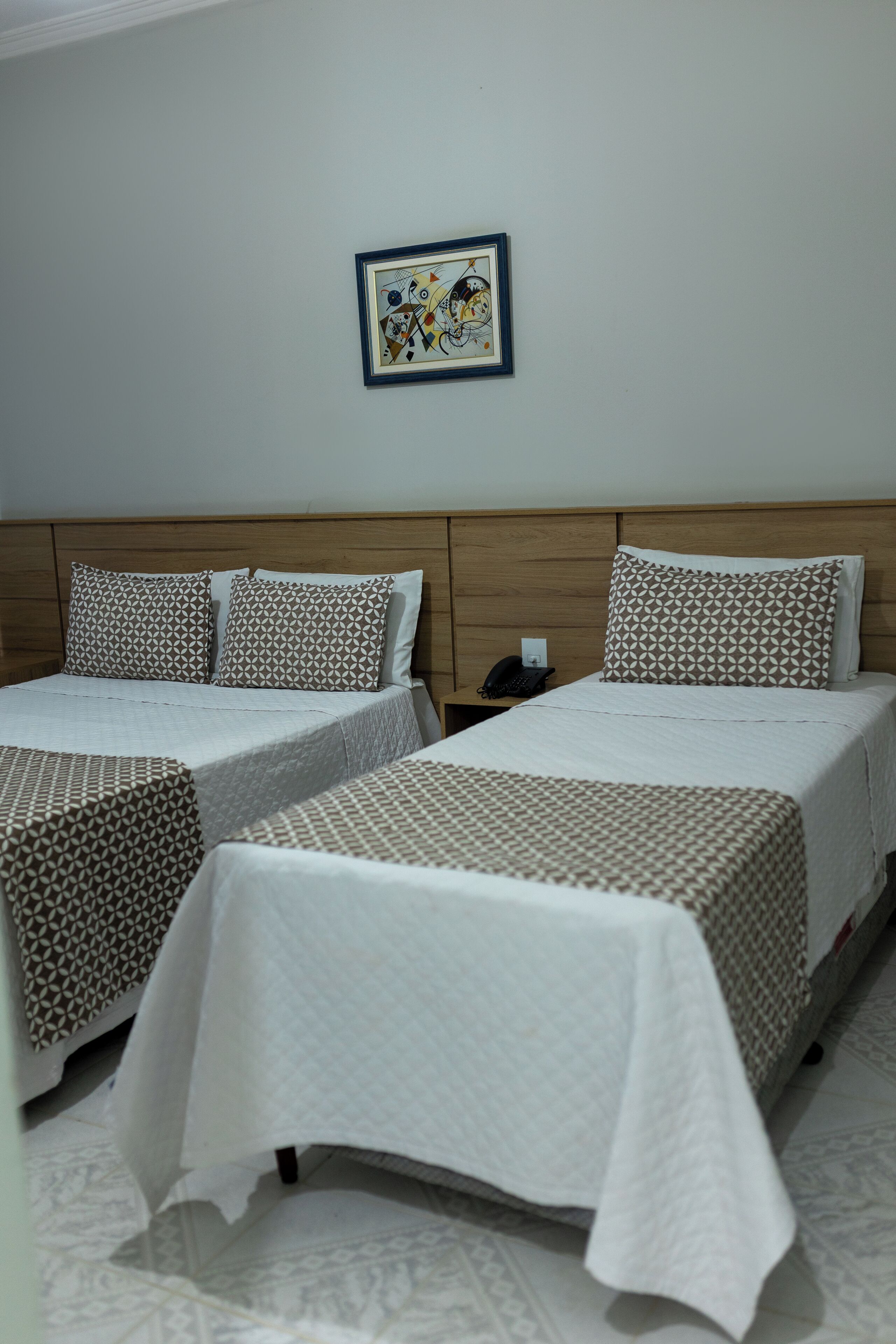 A hotel room with two beds, each with patterned bedding and pillows. There is a framed artwork on the wall above the beds.