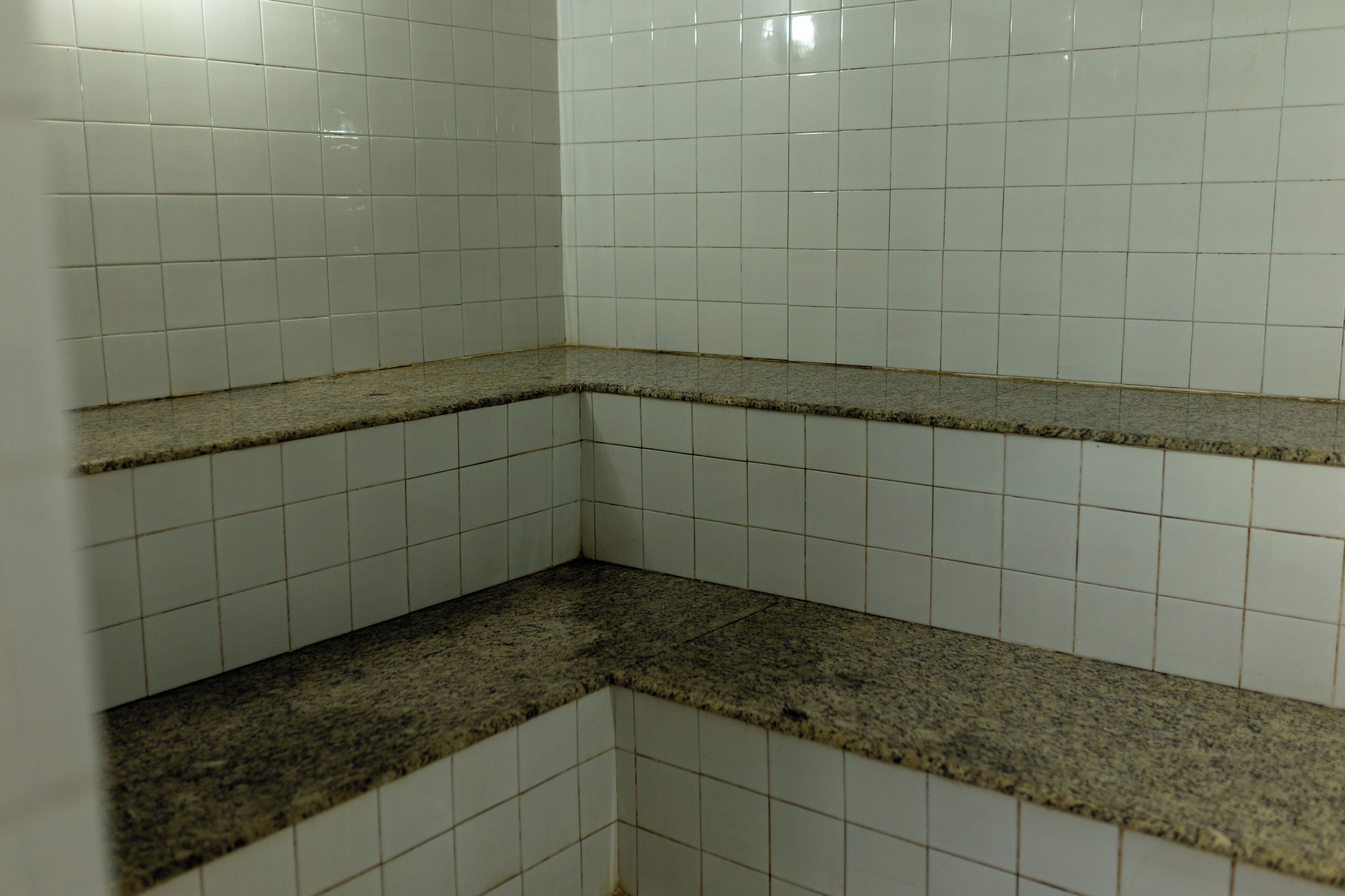 A corner of a room with white tiled walls and a granite countertop.