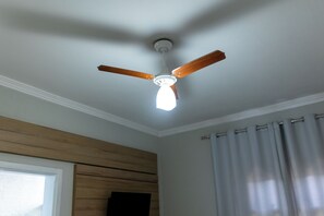 Ein Deckenventilator mit Holzflügeln und einer Lampenleiste in einem Raum mit einer Holzpaneelwand und einem Fenster mit Vorhängen.