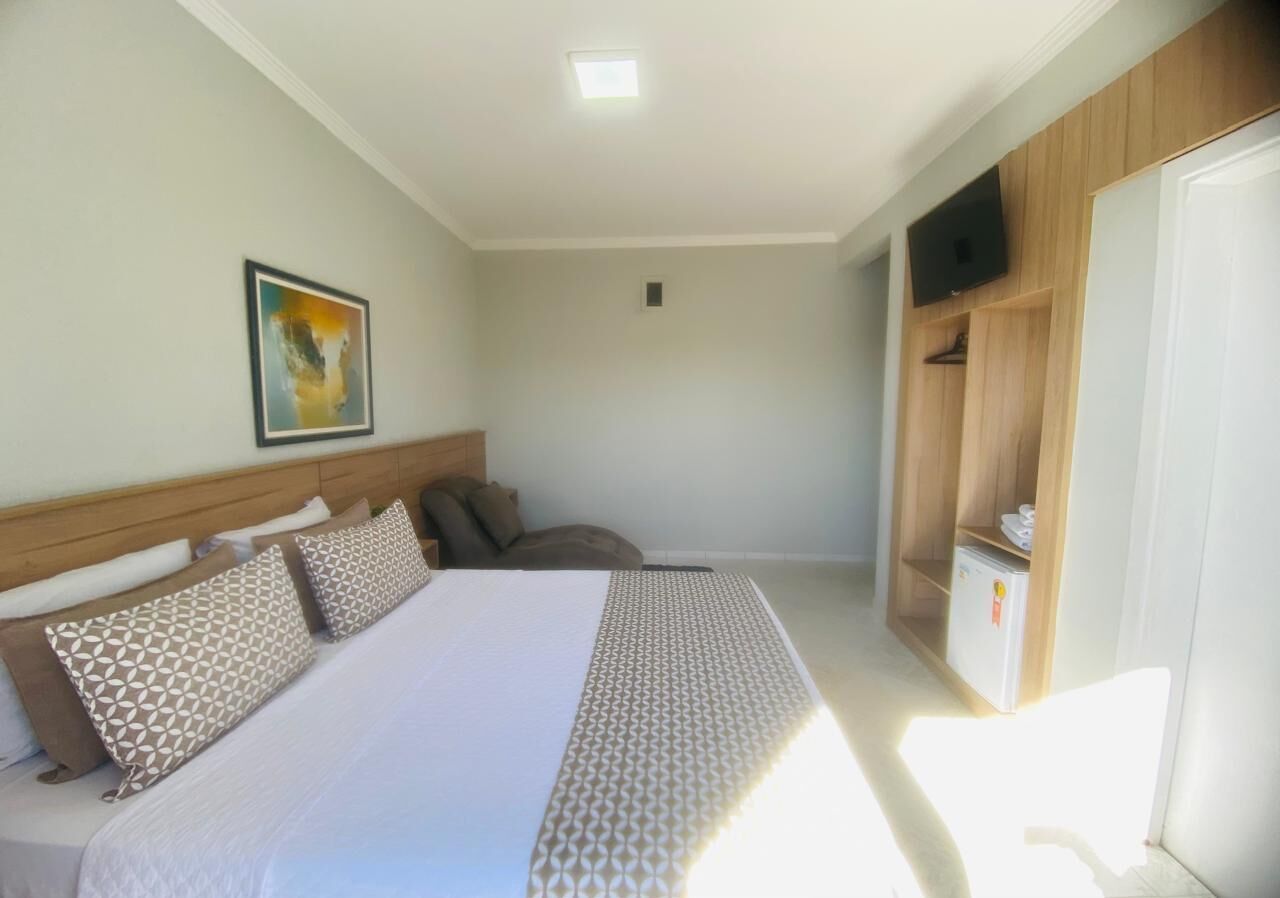 Una habitación de hotel con una cama grande, un cabecero, un televisor en la pared y un armario.