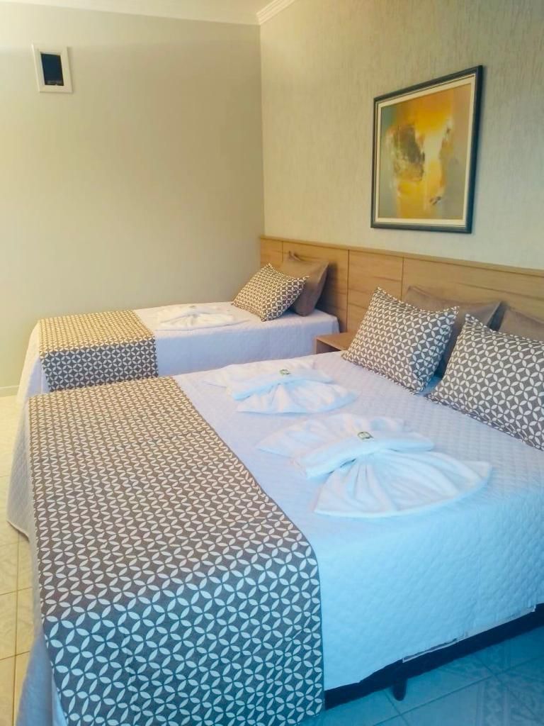 A hotel room with two beds, each with patterned bedding and pillows, a framed artwork on the wall, and a small window.