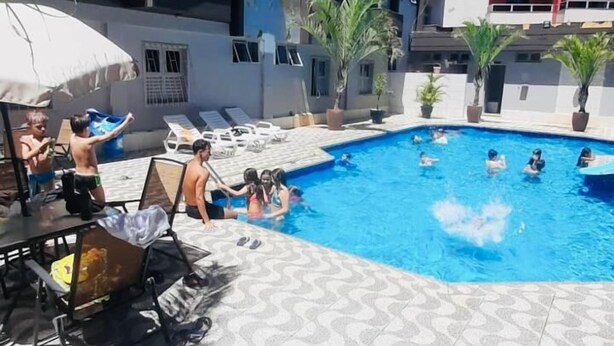 A swimming pool area with lounge chairs and umbrellas, surrounded by a building with balconies. -  JHS Palace Hotel  (Boa Esperança)
