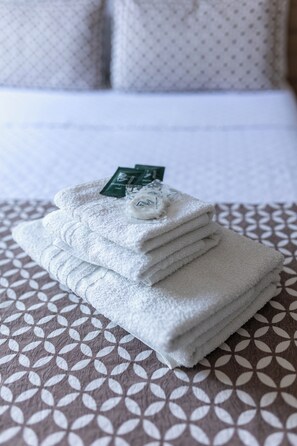 A neatly folded stack of white towels on a patterned bedspread.