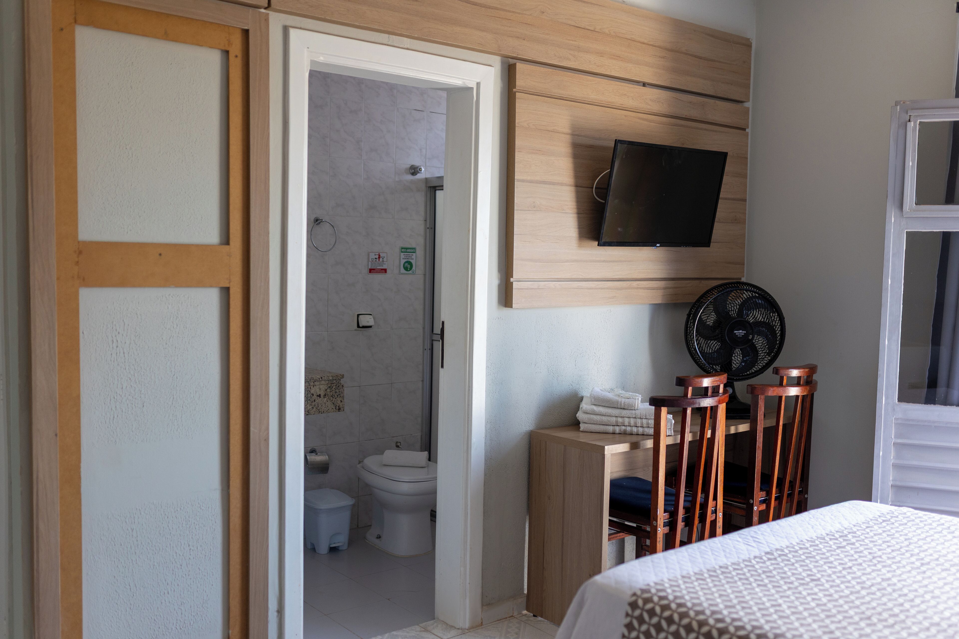 Un dormitorio con cama, televisión montada en la pared, ventilador y un armario de madera.