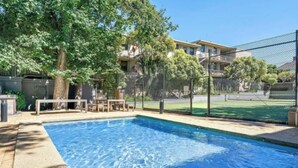 Une piscine dotée d’une terrasse en bois et de chaises, entourée d’une clôture et d’arbres.