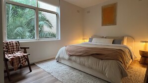 Une chambre à coucher avec un lit, une chaise, une fenêtre donnant sur un paysage verdoyant et un luminaire au plafond.