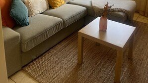 Una sala de estar con un sofá seccional gris, una mesita de centro de madera y una ventana con cortinas.