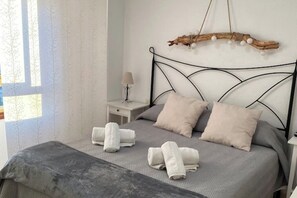 Cama bem arrumada com roupa de cama cinza e duas almofadas, mesa de cabeceira com abajur e um objeto decorativo na parede.