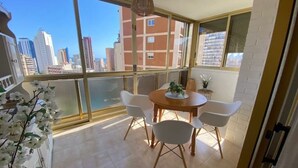 A balcony with a dining table and chairs, large windows, and a view of a cityscape. - CHARMING APARTMENT IN THE HEART OF LEVANTE (Benidorm)
