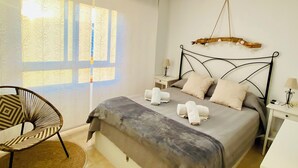 A bedroom with a bed, a chair, a bedside table, a lamp, and a ceiling fan. - CHARMING APARTMENT IN THE HEART OF LEVANTE (Benidorm)