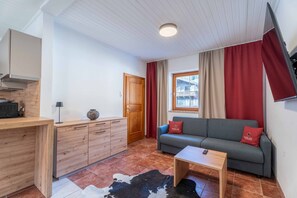 Ett modernt vardagsrum med en soffa, ett soffbord, ett träskåp, en köksdel och ett fönster med gardiner.