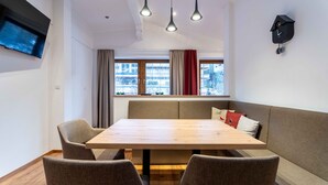 A dining area with a wooden table and four chairs, a bench with cushions, a wall-mounted clock, and a TV on the wall. - KUCKUCK Hinterthal - Top 5 (Maria Alm am Steinernen Meer)