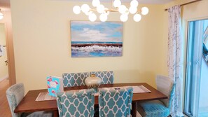 A dining area with a table, chairs, a vase, and a painting on the wall.