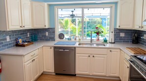 A kitchen with white cabinets, a dishwasher, a sink with a window view, and a wooden countertop.
