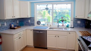Una cucina con mobili bianchi, una lavastoviglie, una finestra vista verde e una ventola a soffitto.