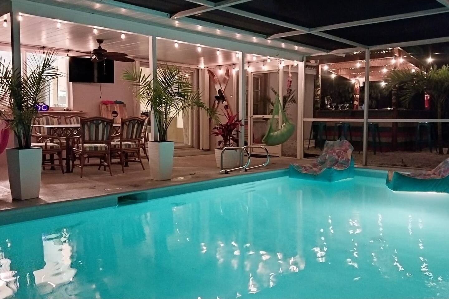 Un área de piscina con sillas y mesas, rodeada de plantas en macetas.