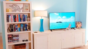 A living room with a bookshelf, a flat-screen TV, a lamp, and a small statue on a white cabinet. - Heated Pool / A Tiki Bar / Near The Beach / Kids & Pet fr. (Fort Myers)