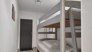 Une chambre avec un lit superposé, une lucarne, une porte et un plancher en bois.