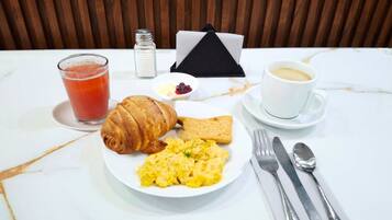 A breakfast setting with scrambled eggs, toast, a croissant, a glass of juice, a cup of coffee, and a salt shaker on a marble table.