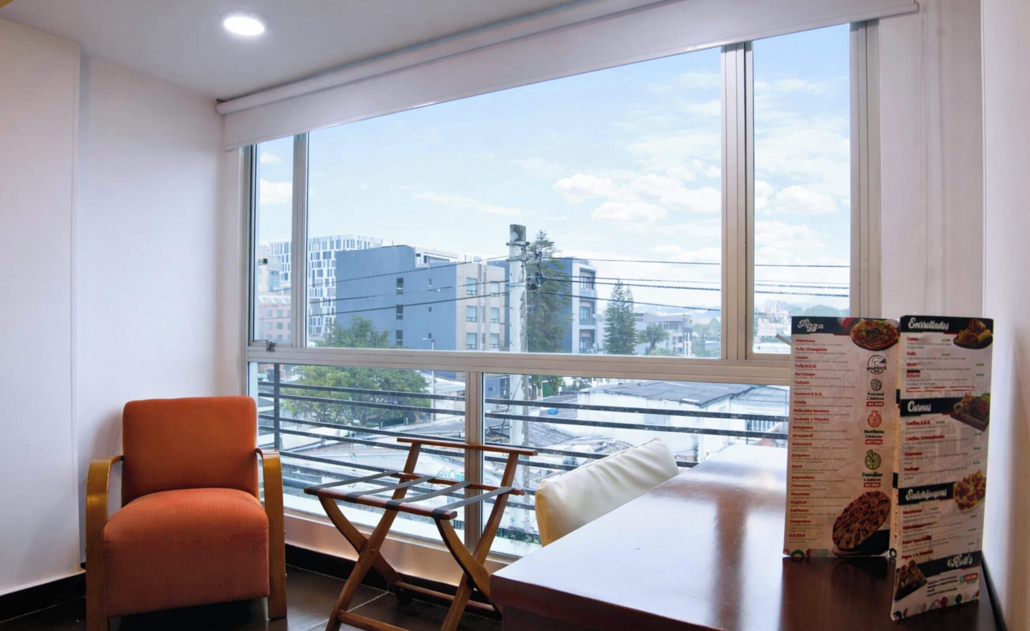 A room with a large window, a chair, a small table, and a menu on the table.