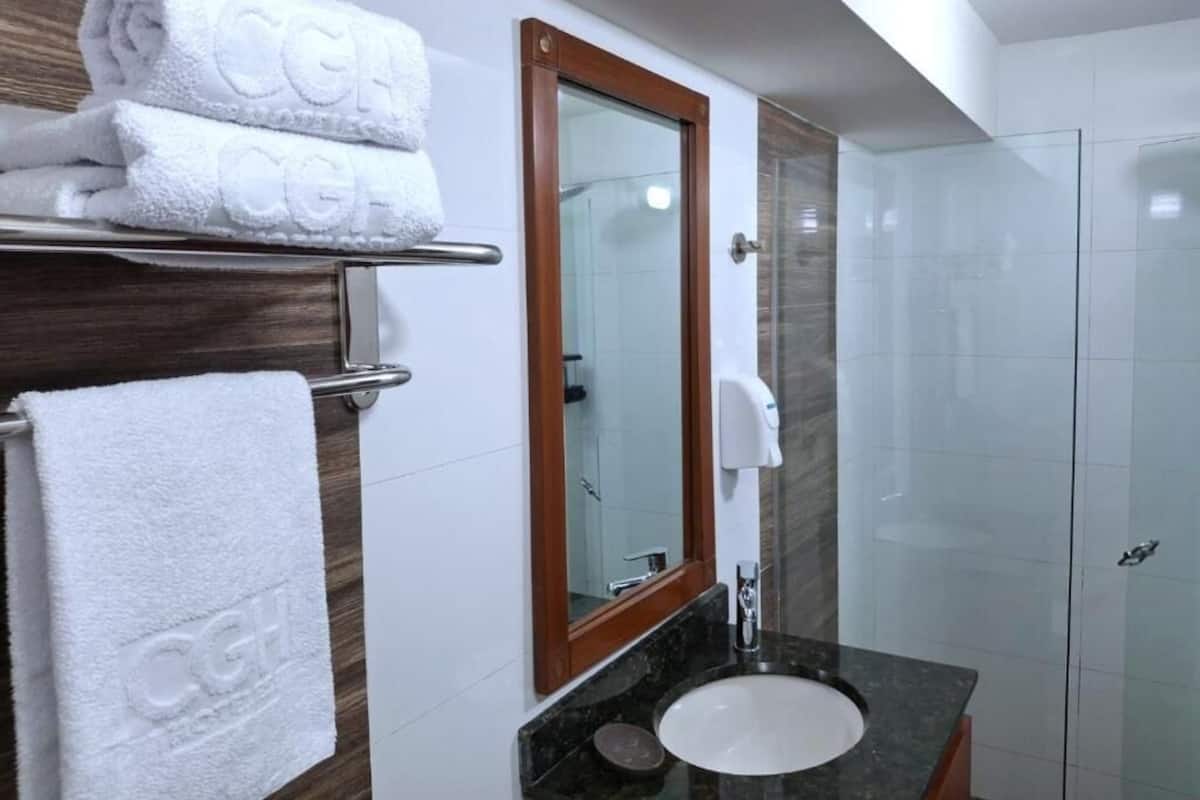 A bathroom with a white sink, a mirror with a wooden frame, a towel rack with towels, and a glass shower enclosure.