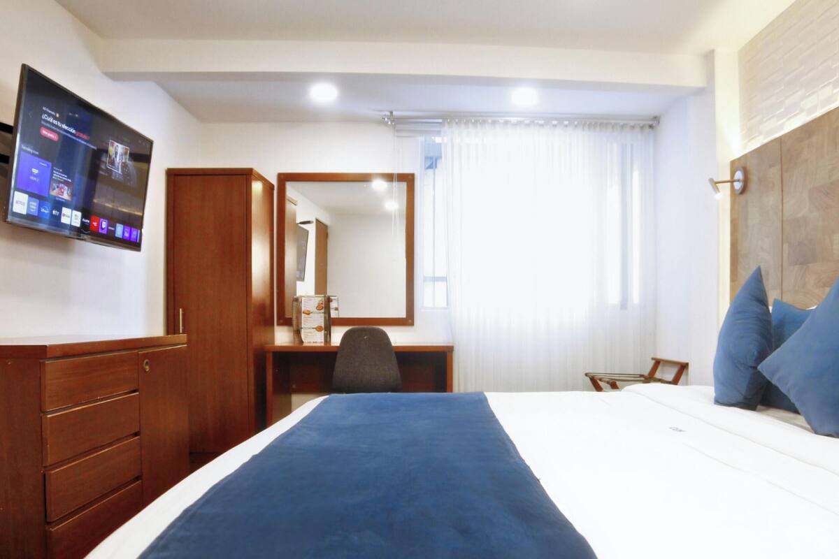 A hotel room with a bed, a desk, a chair, a television, and a mirror.