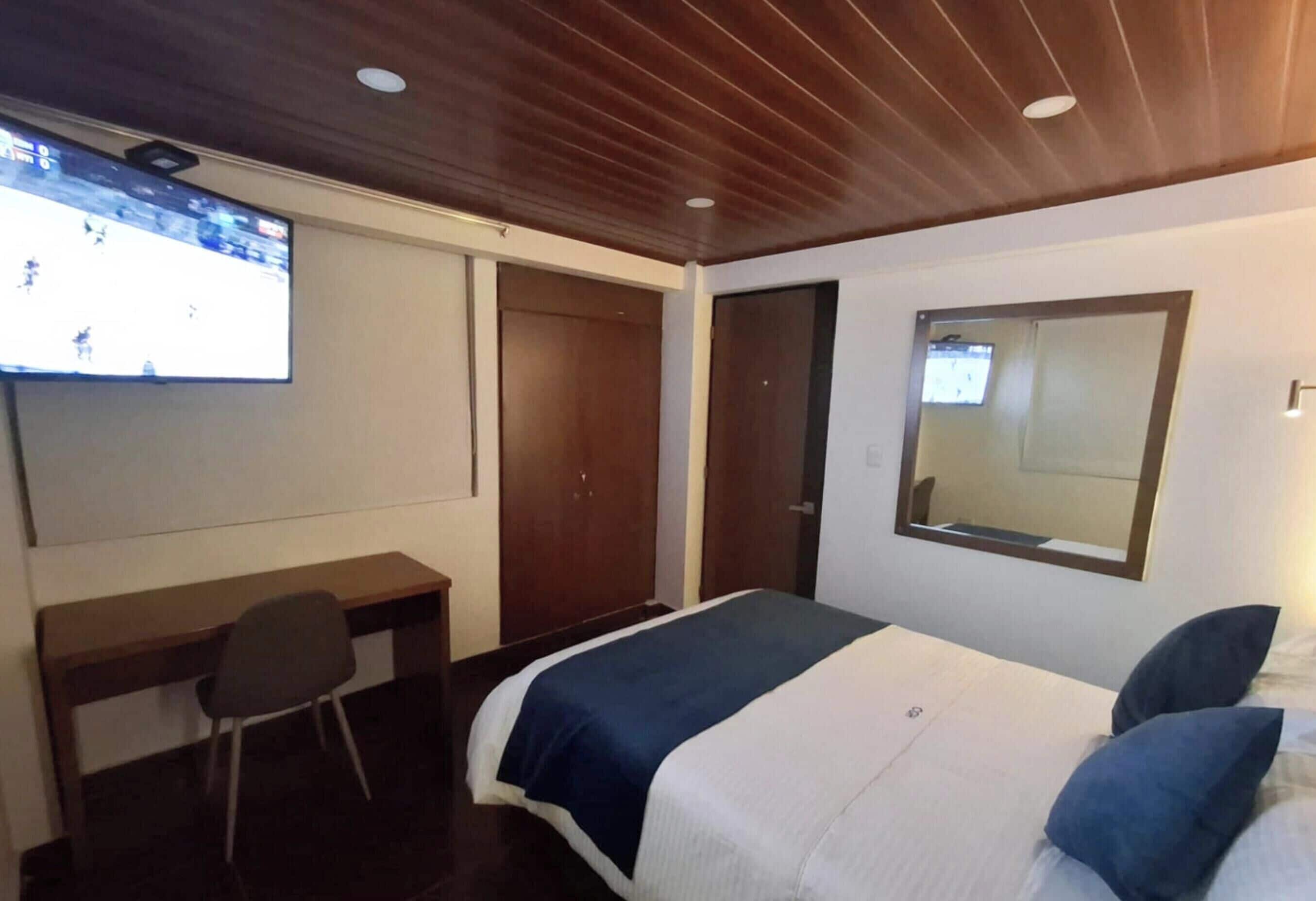 Una habitación de hotel con cama, escritorio, silla, televisor y espejo.