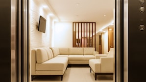 A modern elevator with a metallic finish, a beige sectional sofa, and a wooden partition. - Hotel CGH Travel INN Aeropuerto (Bogota)