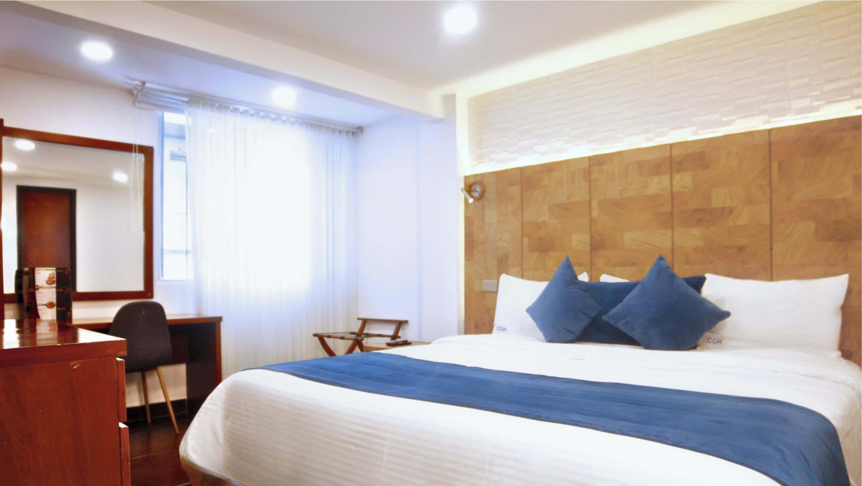 A hotel room with a bed, a desk, a chair, a mirror, and a window with curtains.