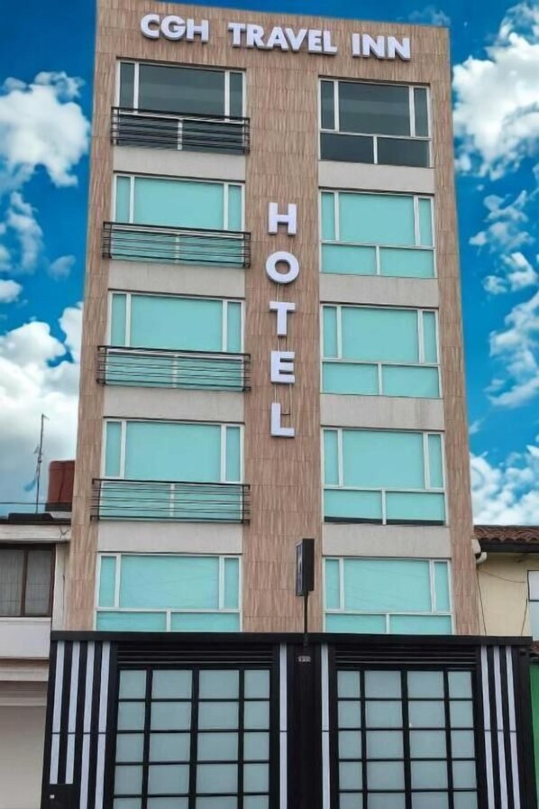 Un hotel CGH Travel Inn con una facciata moderna, numerose finestre e un cancello d'ingresso ben visibile.