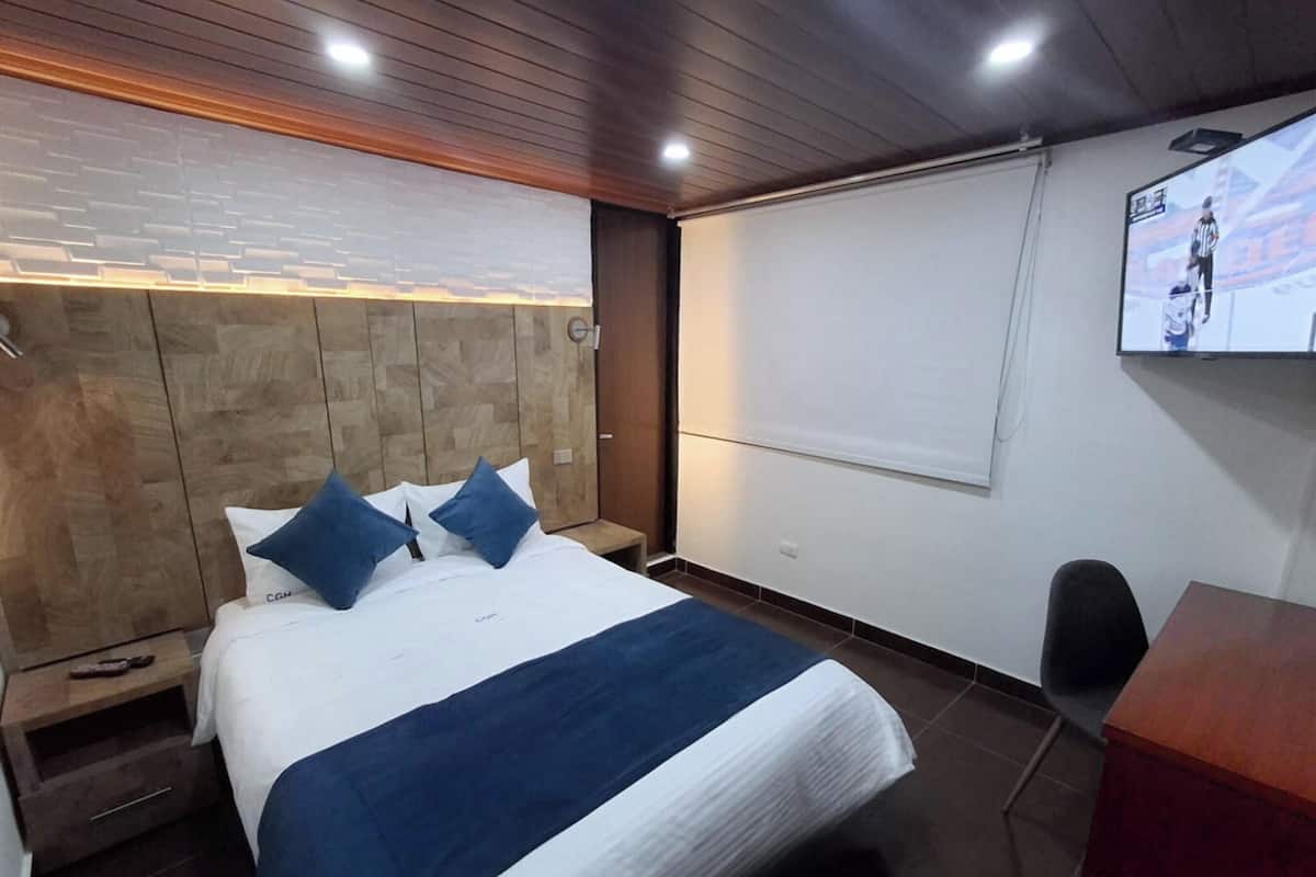 A hotel room with a bed, a TV, a desk, and a chair.