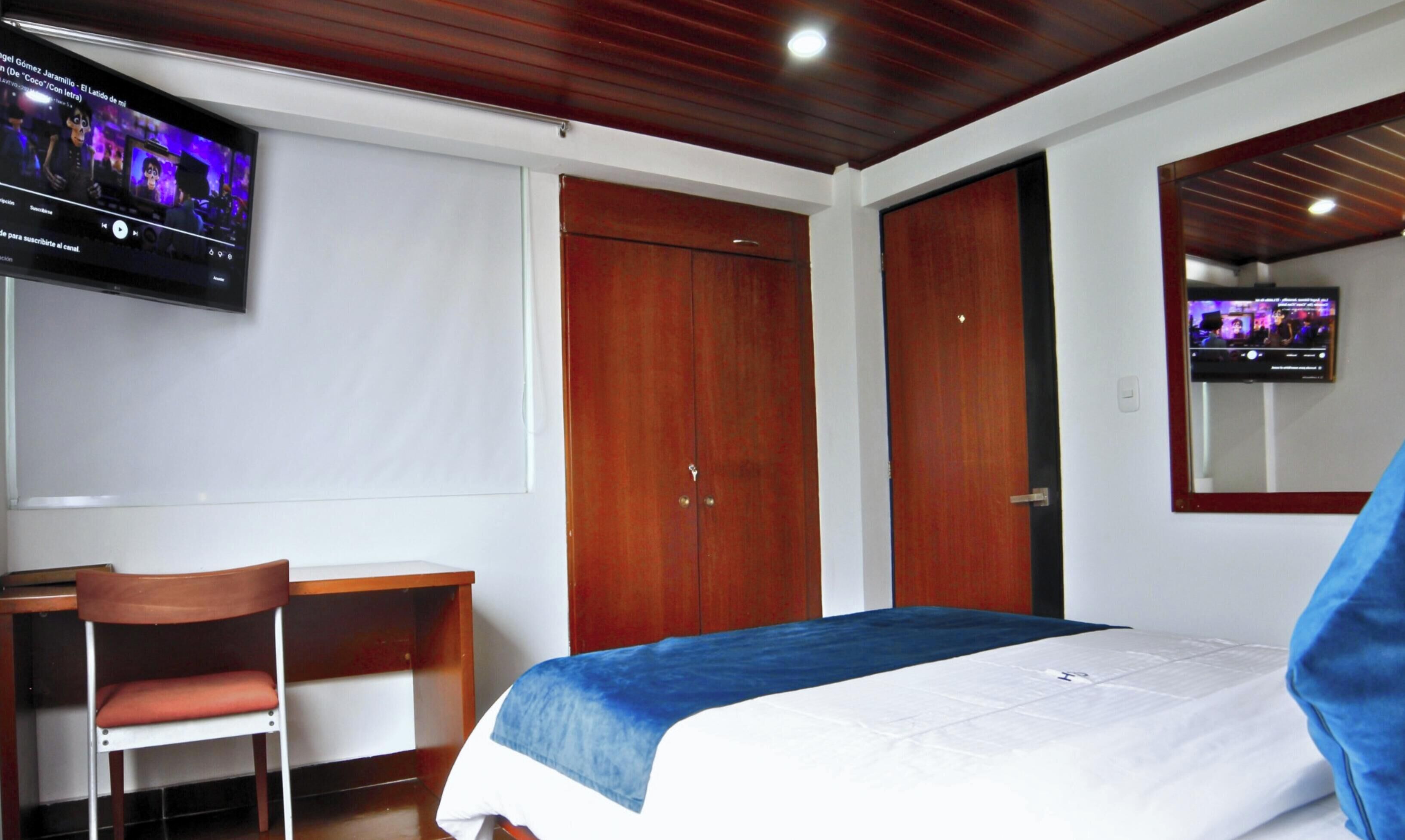 A hotel room with a bed, a desk, a chair, a television, and a wardrobe.