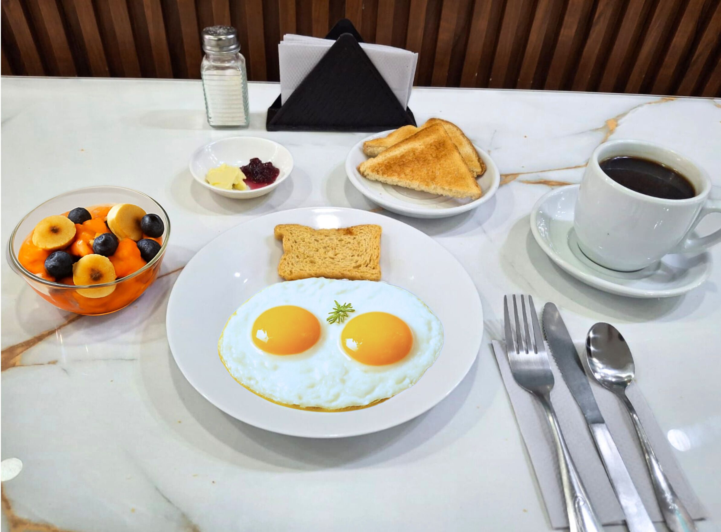 A breakfast setting with eggs, toast, fruit, and coffee on a marble table.
