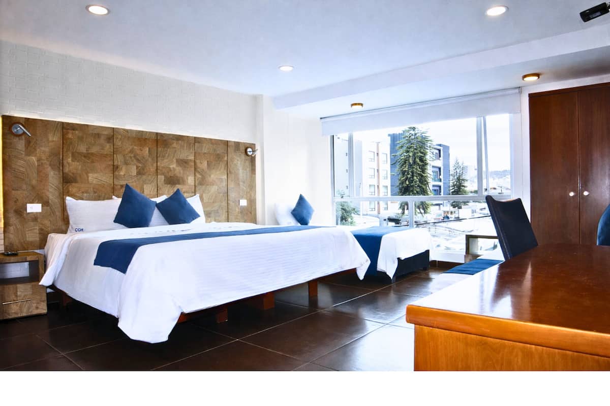 A hotel room with a large bed, a desk, and a view of buildings through the window.