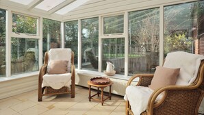 Une véranda avec des fauteuils en osier, une petite table et de grandes fenêtres donnant sur le jardin.