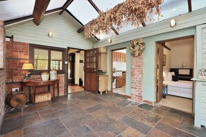A spacious hall with a high ceiling, stone flooring, and wooden beams. There are multiple doors leading to different rooms, a table with a lamp, and a basket on the floor. - Peaceful Rural Escape for 11 •  Fires, BBQ, Pet Friendly • Large Kitchen • Great for Multi-Generational Families  • (Pencombe)