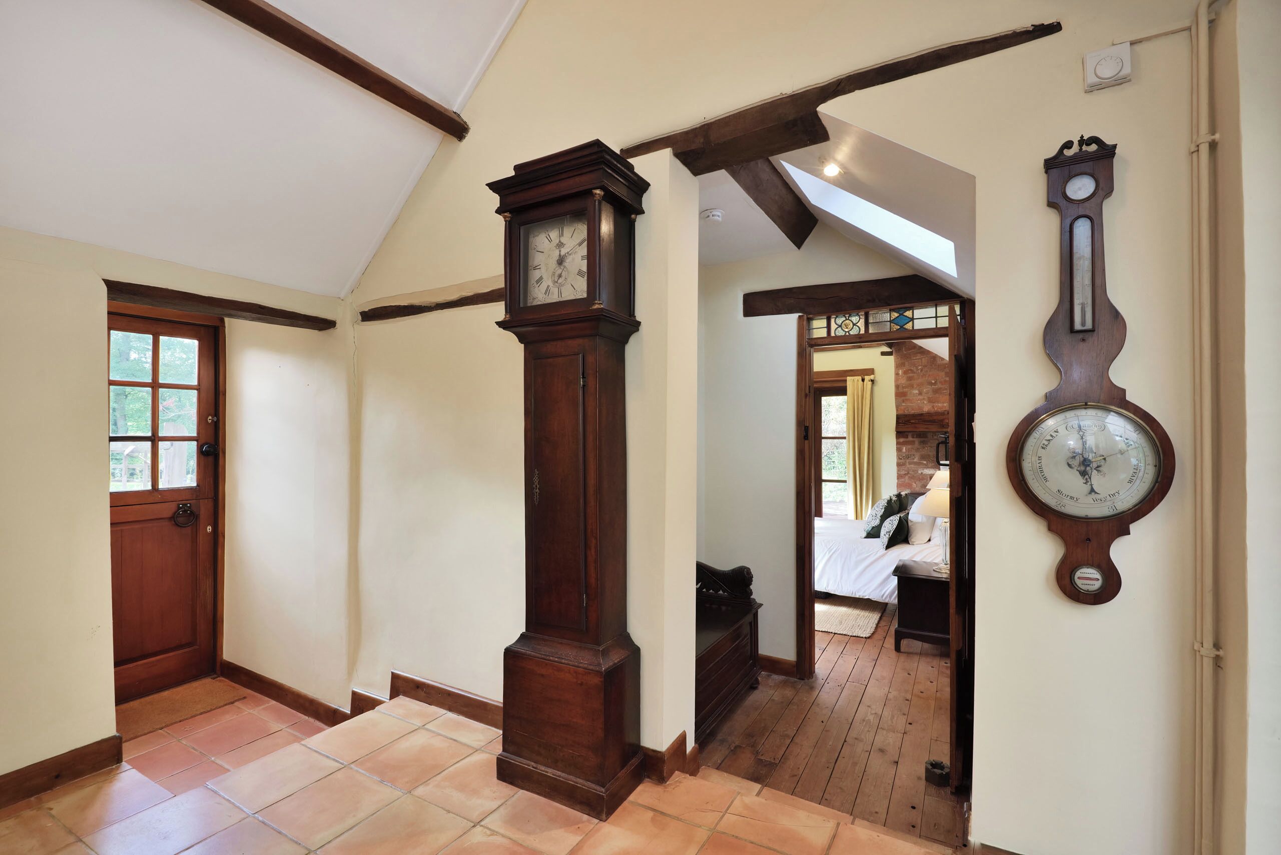 Un pasillo con piso de madera, un reloj de pie grande y un reloj de pared tipo brújula.