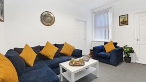 A living room with a sectional sofa, a coffee table, and a wall clock. - Cosy 2-Bedroom Apartment, comfortably sleeps 5 (Gateshead)