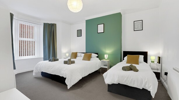 A hotel room with two beds, a window with curtains, a green accent wall, and framed artwork. - Cosy 2-Bedroom Apartment, comfortably sleeps 5 (Gateshead)