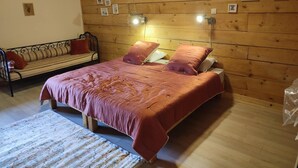 Un dormitorio acogedor con techo de madera, una cama con ropa de cama rosa, un banco de madera y cuadros enmarcados en la pared.