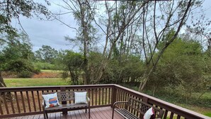 A wooden deck with benches and a view of a grassy area and trees. - Owl's Nest, a rustic tiny house located 3.5 miles off I-65 in Evergreen, Alabama (Evergreen)